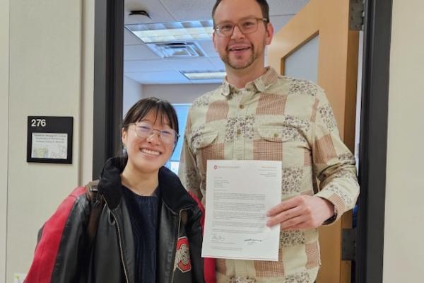 A man stands next to a woman while displaying a letter on University letterhead