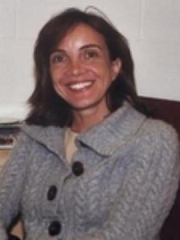 a seated woman wearing a gray sweater smiles at the camera