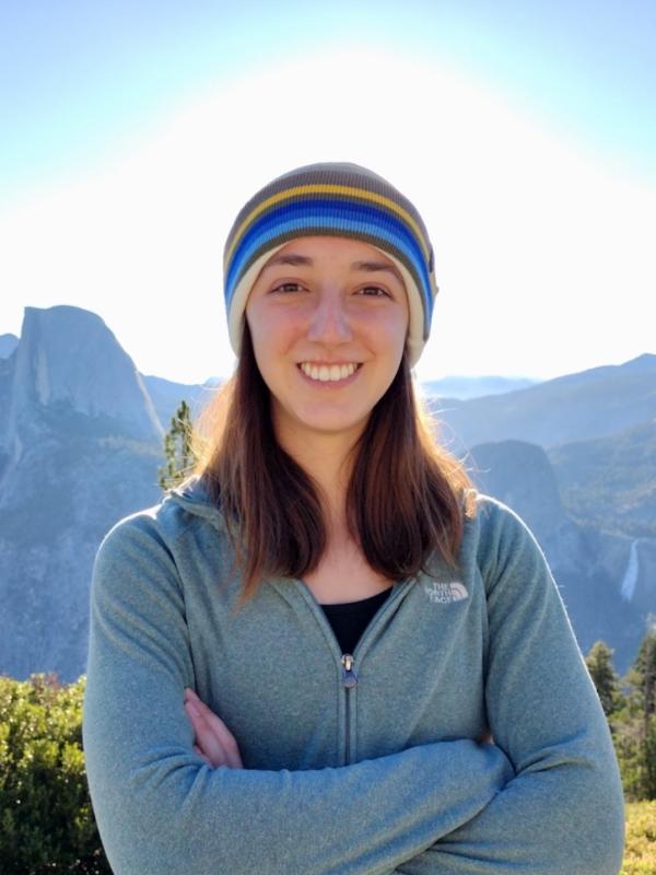 A woman stands in front of trees and mountains